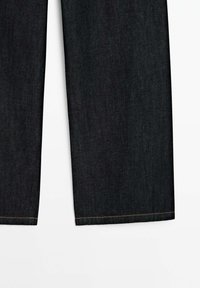 Tmavé denimové kalhoty s rovnými nohavicemi, kontrastním prošíváním a čistým lemem. Materiál má hladkou texturu s jemným leskem.