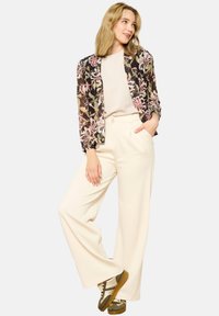 Floral print jacket in black with pink and green accents, paired with cream wide-leg trousers and olive sneakers. Smooth textures and relaxed fit.