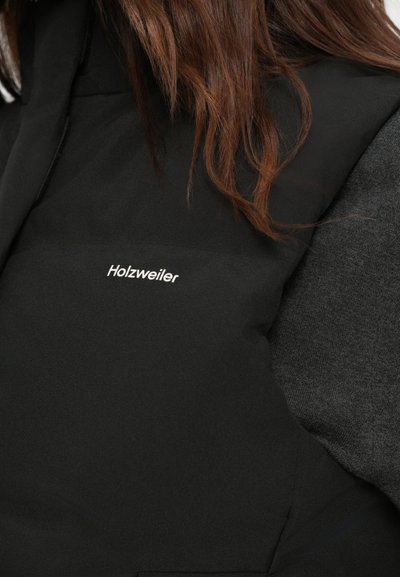 Gilet in piuma nera con accenti grigi. Presenta una texture liscia e un logo sottile "Holzweiler" in bianco sul lato sinistro anteriore.