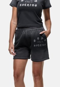 Shorts noirs en tissu doux avec une taille élastique, dotés de poches latérales et d'un texte graphique blanc sur le devant.