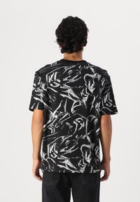Short-sleeve black t-shirt featuring a white abstract pattern. Round neckline, relaxed fit, and soft texture with logo detail at the hem.