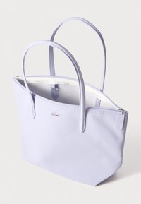 Ljust lila tote-väska med en strukturerad form, slät yta, två axelremmar och blixtlåsöppning med en liten logotypdetalj.