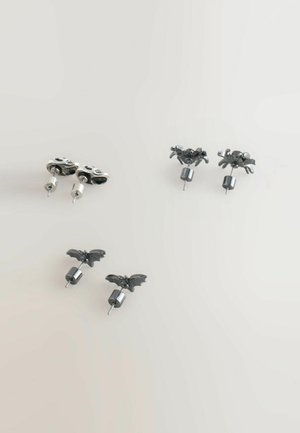 Boucles d'oreilles en argent en forme de crâne avec des accents noirs et des designs en forme de chauve-souris. Deux paires exposées, remarquables pour leur détail complexe et leur texture.