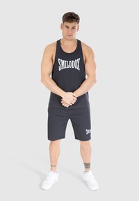 Czarny zestaw składający się z tank topu i szortów z białym logo "SMILODOX". Materiał wydaje się gładki; bezrękawnik o luźnym kroju. Białe buty sportowe.