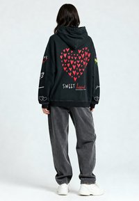 Must värvi südameprindiga must kapuutsiga särk, tekst "SWEET heart" ja graafilised üksikasjad varrastes. Kanda hallide pükstega ja valgete kingadega.