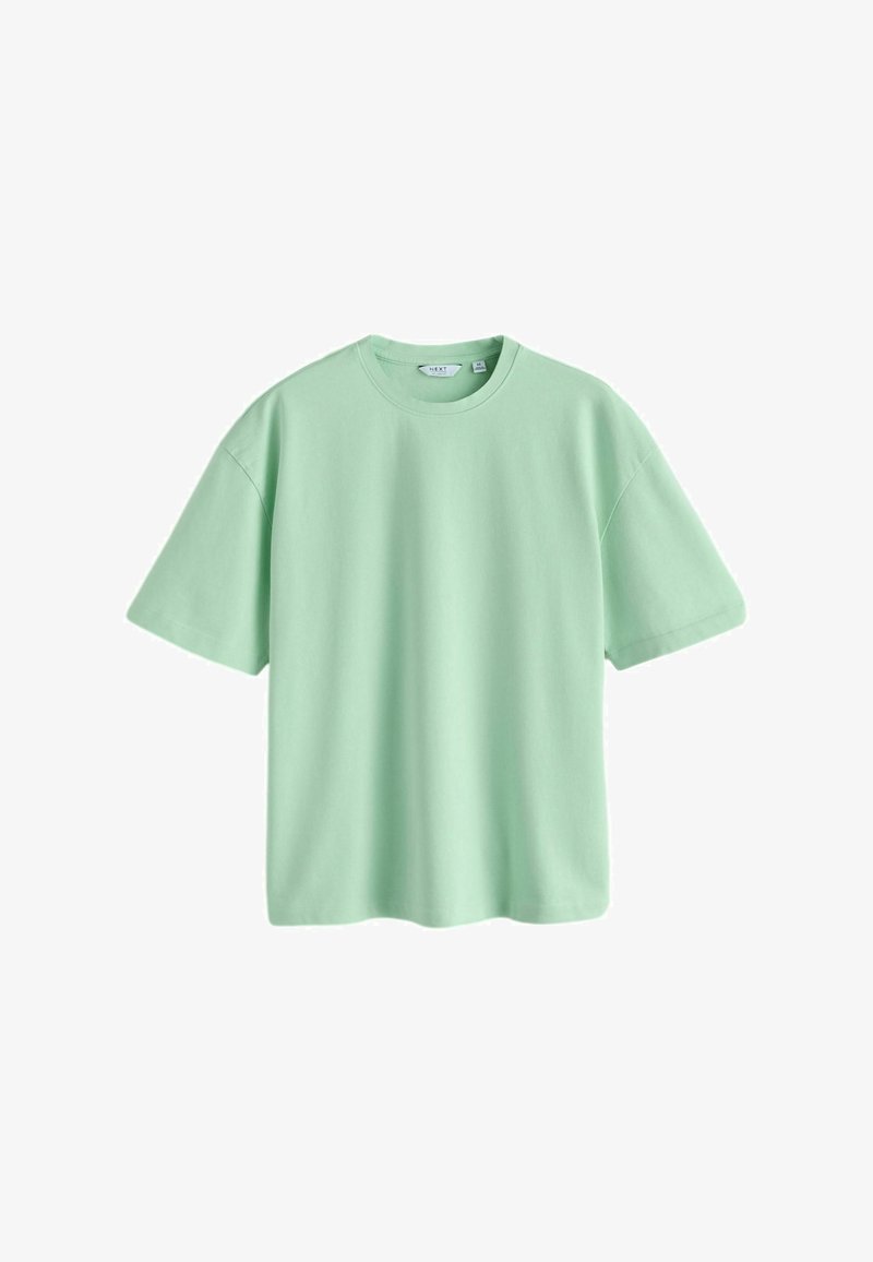 T-shirt vert clair en coton à manches courtes, col rond, coupe ample, avec une étiquette visible au niveau du col.