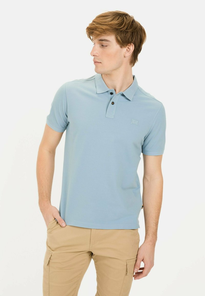 Lichtblauw poloshirt met korte mouwen van gladde stof, voorzien van een drieknoopsluiting en een klein logo op de borst, gecombineerd met beige cargobroeken.