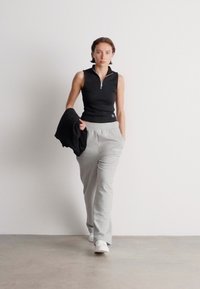 Czarny bezrękawnik na zamek, szare dresy, białe trampki i czarna bluza przewieszona przez ramię. Gładkie faktury, prosty design.