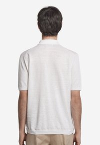 Vit kortärmad polo av lättviktsmaterial, med ribbad krage och ärmslut, samt en enkel, strukturerad design på baksidan.