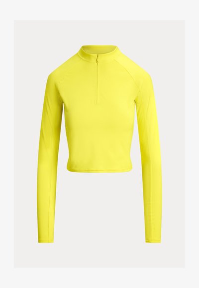 Κίτρινο crop top με μακριά μανίκια, που διαθέτει ψηλό γιακά και ημιδιαφανή φερμουάρ. Λείο, ελαστικό ύφασμα με ελάχιστες ραφές και εφαρμοστή σχεδίαση.