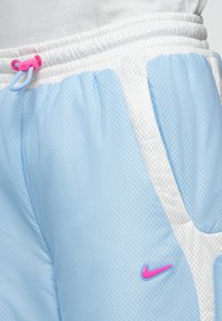 Svetlo modré športové šortky s bielymi akcentmi, sieťovanou textúrou, elastickým pásom a ružovým šnúrkou. Na prednej strane sa nachádza ružové logo Nike.