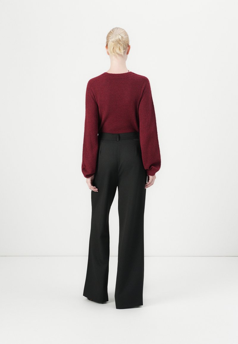 Burgunderfarbener Strickpullover mit Ballonärmeln, kombiniert mit schwarzen, hoch taillierten weit geschnittenen Hosen. Strukturierter Stoff mit schlichter Gestaltung.