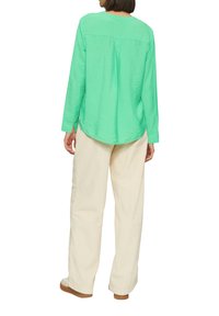 Groene longsleeve shirt met een textuurafwerking, ronde zoom en een plooi aan de achterkant, gecombineerd met lichtbeige broeken en casual schoenen.