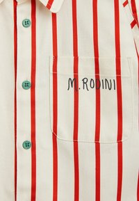 Koszula z krótkim rękawem w kolorze kremowym z pionowymi czerwonymi paskami, turkusowymi guzikami oraz kieszonką na piersi z odręcznym napisem "M. RODINI."