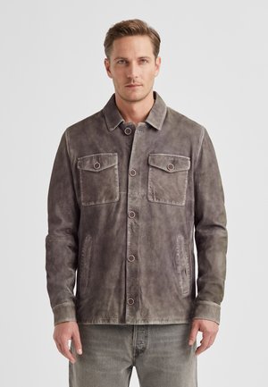 Graue Wildlederjacke mit durchgehender Knopfleiste, zwei Brusttaschen und Seitentaschen. Mit spitzem Kragen und strukturierter Oberfläche.