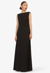 Black sleeveless gown with a boat neckline and floor-length silhouette, featuring a smooth texture and minimalistic design.