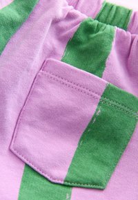 Cotton fabric in pink with green vertical stripes, featuring a small pocket. The texture appears soft with visible stitching details.