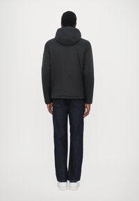 Schwarze Kapuzenjacke mit glatter Textur, von hinten gezeigt, kombiniert mit dunklen Jeans und weißen Schuhen. Einfaches Design ohne Muster.