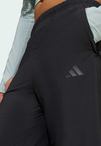 Black athletic pants with an elastic waistband, featuring a sleek texture and a subtle three-stripe logo on the side.