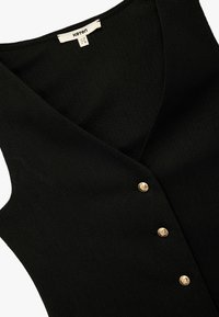 Top negro sin mangas con escote en forma de V, que presenta una textura acanalada y tres botones dorados en el frente. Etiqueta de la marca visible.