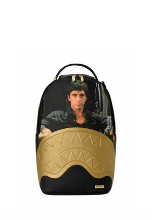 Zaino nero e oro con un'immagine stampata di un uomo serio con una camicia nera seduto dietro un motivo dorato curvo.