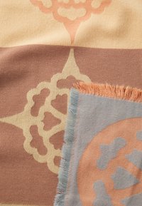 Tessuto intrecciato con motivi beige e terracotta. Un angolo presenta un bordo blu con dettagli sfilacciati e un design circolare arancione.