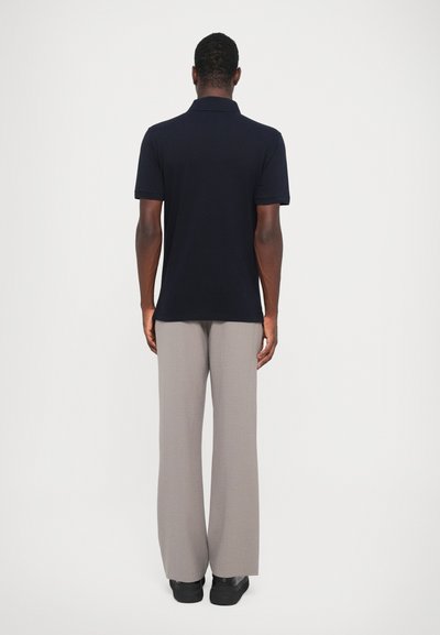 Jūras spēku polo krekls ar klasisku apkakli, apvienots ar gaiši pelēkiem platām biksēm, valkāts ar melnām kurpēm, skatīts no aizmugures.