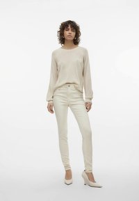 Pulover crem cu dungi, cu mâneci lungi, asortat cu blugi skinny deschiși la culoare, cu talie înaltă, și pantofi albi cu vârf ascuțit.