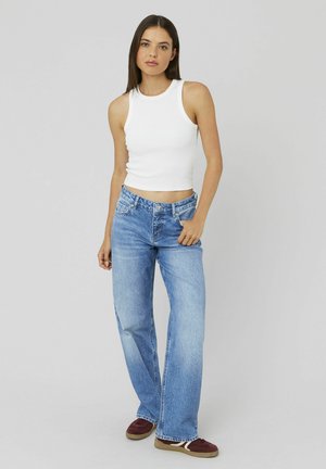 Un haut débardeur blanc ajusté associé à un jean large bleu clair. Le jean a une taille haute et un ourlet effiloché, complété par des chaussures rouge foncé.