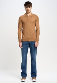 Polo de manga larga en color beige con textura acanalada y cierre de tres botones, combinado con unos pantalones vaqueros azules y zapatillas marrones. Diseño sencillo y ajustado.