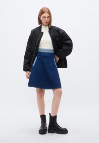 Μαύρο μπουφάν bomber, λευκό ριμπ μπλουζάκι, μπλε τζιν φούστα Α-γραμμή με δύο πλαϊνές τσέπες και μαύρα μποτάκια με πλατφόρμα στον αστράγαλο. Λείο υλικό, καθημερινό στυλ.