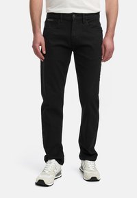 Jeans de mezclilla negra con un diseño de corte recto, cinco bolsillos, cierre frontal con botón y detalles de costura sutiles, llevados con zapatillas blancas.