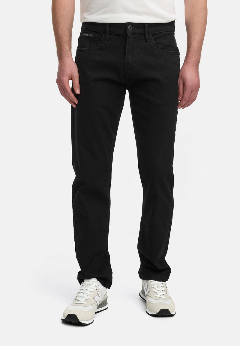 Jeans de mezclilla negra con un diseño de corte recto, cinco bolsillos, cierre frontal con botón y detalles de costura sutiles, llevados con zapatillas blancas.