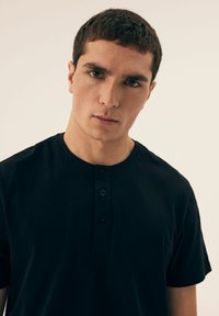 Black short-sleeve shirt with a rounded neckline and three-button placket. Smooth, cotton fabric with no visible patterns or accents.