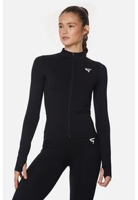 Schwarze sportliche Zip-up-Jacke aus glattem, dehnbarem Material. Mit langen Ärmeln mit Daumenlöchern und einem kleinen Logo auf der linken Brust.