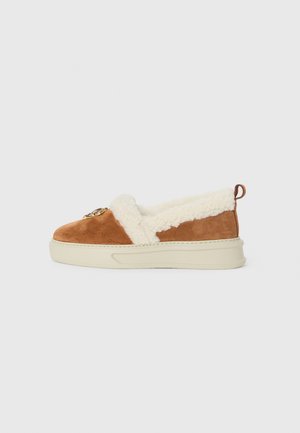 Chaussure slip-on en suède marron avec doublure et détail en fausse fourrure crème. Semelle blanche épaisse et petite boucle au talon pour un enfilage facile.