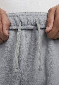 Pantalones deportivos de felpa gris con cintura elástica, que cuentan con un cordón para ajuste y una superficie suave y texturada.