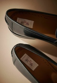 Crne kožne mokasine s elegantnim dizajnom, glatkom teksturom i unutarnjom oznakom koja glasi "NEXT SIGNATURE ITALIAN LEATHER".