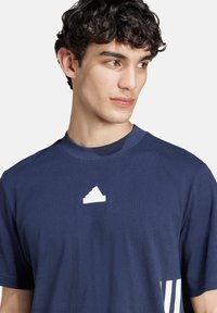 T-shirt in cotone blu navy con maniche corte, con il logo bianco di Adidas sul petto e tre strisce bianche sul lato.