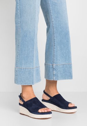 Sandales compensées en suede bleu marine avec orteils et talons ouverts, présentant une plateforme en jute, portées avec un jean large bleu clair.