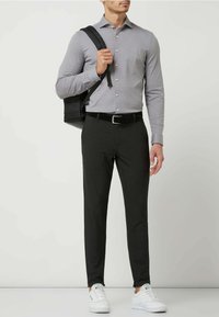 Graues Buttons-Hemd, schwarze Hose, weiße Sneaker; schwarzer Rucksack über der Schulter; glattes Material, taillierte Passform und kontrastierende Farben.