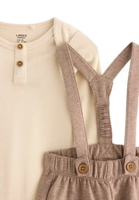 Beige pruhovaný top s dlouhým rukávem a dvěma dřevěnými knoflíky. Hnědé elastické kalhoty s bočními knoflíky a jemnou texturou, vhodné pro kojence.