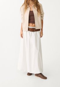 Beżowa zapinana na guziki kurtka, brązowy krótki top, biała długa spódnica maxi, brązowy pasek z ćwiekami, brązowe trampki z siateczkowymi wstawkami.