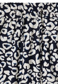 Pantalon bleu marine avec imprimé léopard abstrait blanc et bleu clair, taille élastique et cordon assorti avec œillets argentés.