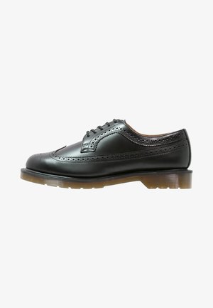 Czarny skórzany but brogue z wzorem typu wingtip, perforowanymi detalami, czarnymi sznurowadłami oraz grubą, półprzezroczystą, brązową gumową podeszwą.