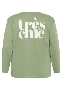 Majica dugih rukava svijetlozelene boje izrađena od pamuka, koja na leđima ima veliki, odvažan bijeli grafički tekst "très chic".