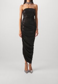 Černé midi šaty bez ramínek s drapérií, vyrobené z lesklé tkaniny. Oblečené s stříbrnými vysokými podpatky a masivným stříbrným náhrdelníkem.
