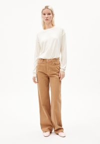 Beige long-sleeve top paired with light brown wide-leg corduroy pants. The ensemble features a relaxed fit and minimalist design. Pink shoes complete the look.