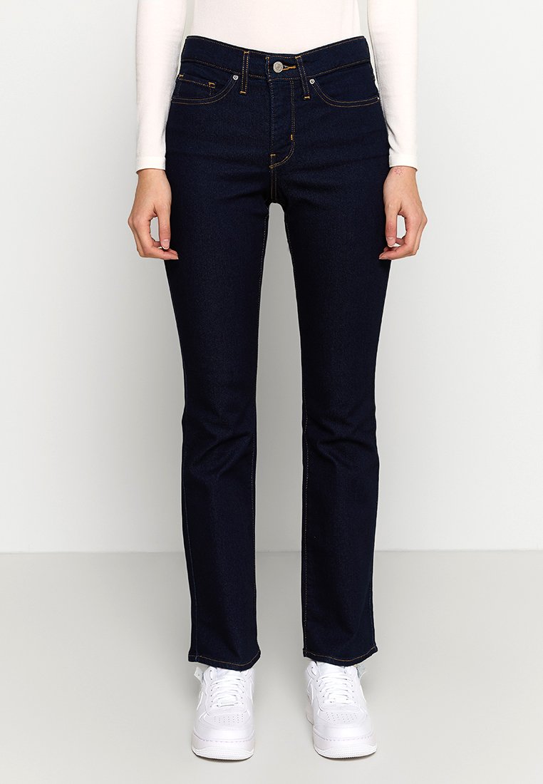 Mørkeblå denimjeans med lige ben-design, prydet med orange syninger, fem lommer og en mid-rise talje, kombineret med hvide sneakers.