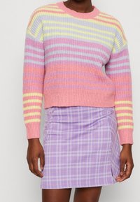 Pull en tricot multicolore avec des rayures horizontales rose, violet, jaune et gris. Associé à une mini-jupe à carreaux lavande.
